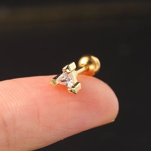 Macro detail of golden stud earring with triangle zircon held on a fingertip