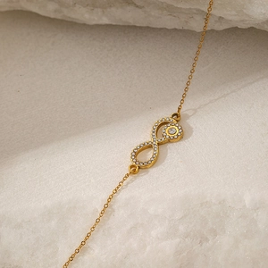 Close-up of golden infinity pendant necklace with cubic zirconia on a white stone background