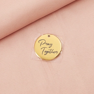 Macro detail of golden stainless steel round pendant with Pray Together engraving