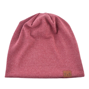 Detail of a dark red knit beanie featuring a brown leather patch with F&S text engraving