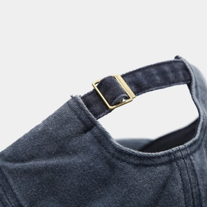 Detailed macro view of the vintage bronze buckle on a washed denim baseball cap