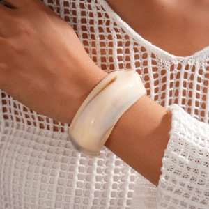 Close-up of wide cream acrylic cuff bracelet on wrist with elegant knit background
