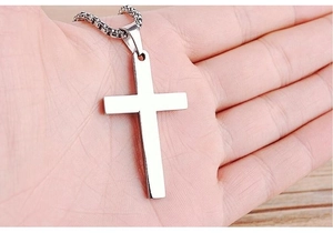 Close-up of minimalist silver cross pendant held in hand showing smooth polished metal surface