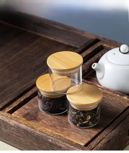 Three mini glass tea canisters with bamboo lids and silicone seals on a wooden tray