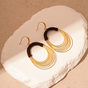 Detail of layered gold metal hoops with brown fabric wrapping on a textured stone base