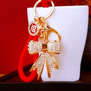 Close-up of golden metal bow keychain with rhinestones and red woven rope detail