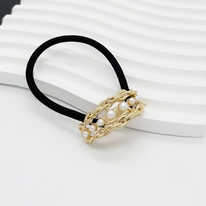 Detail of elegant black hair tie with gold chain link and white pearl inlay on white stand