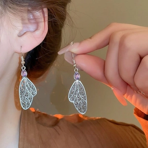 Detailed view of silver hollow wing earrings with a purple teardrop gemstone on model