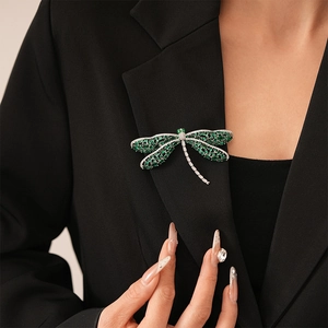 Detailed view of a dragonfly brooch with green marquise gems on a black blazer