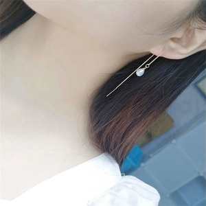 Detail view of long gold chain tassel earrings with drop-shaped white pearl on model