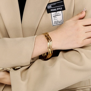 Detailed view of layered gold wave bracelet on model wrist with elegant suit sleeve