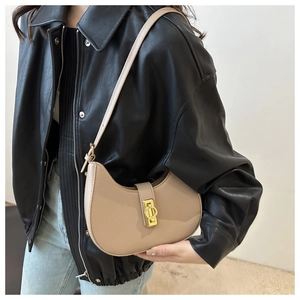 Detail of beige crescent underarm bag with gold hardware worn with a black leather jacket