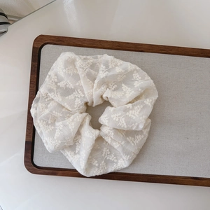 Close-up of white lace scrunchie with intricate floral embroidery on fabric texture