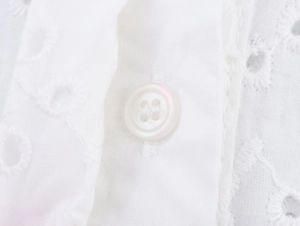 Κοντινό πλάνο λευκής μπλούζας με κέντημα eyelet και ασορτί κουμπί από ρητίνη