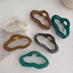 Irregular shaped hair claws in assorted matte colors on a minimalist textured background