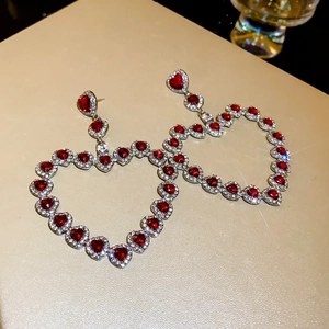 Silver heart-shaped hoop earrings with red gemstone inlay on beige textured background