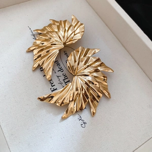 Detail of gold fan-shaped earrings with textured surface on a white jewelry cloth