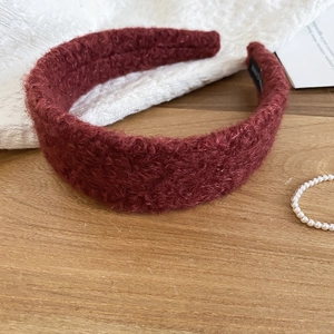 Detail of burgundy plush headband with sherpa texture on a wooden surface with pearls