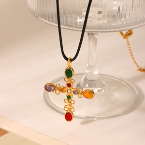 Macro view of a gold cross pendant set with colorful gemstones on a black cord