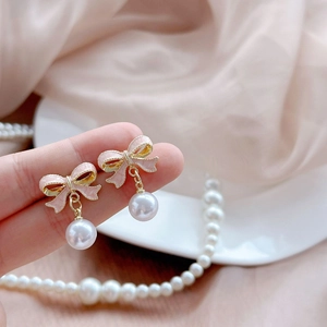 Elegant pink bow earrings with hanging round pearls shown on fingers over pink silk