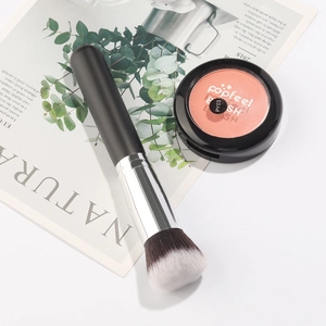 Detail of round head powder brush with soft fibers next to a coral pink blush compact