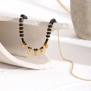 Elegant beaded necklace with black faceted crystals and golden disc charm on white pedestal