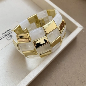 Detail of square acrylic marble and golden metal geometric cuff bracelet on a tray