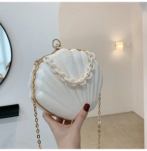 Detail of white shell-shaped acrylic handbag with gold metal frame and thick chain strap