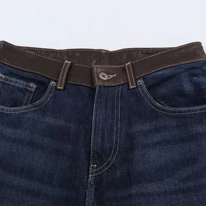 Détail d'un jean bleu foncé avec taille en cuir marron et bouton métallique argenté poli