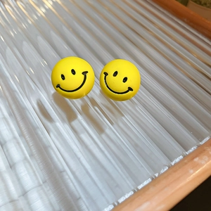 Detail view of cute yellow smiley face stud earrings on a glass tray with wooden frame