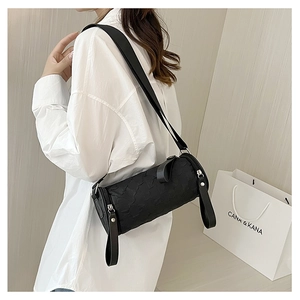 Detail of black cylindrical crossbody bag featuring wide strap and quilted texture