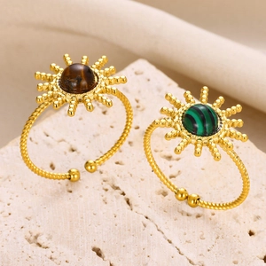 Détail de bagues soleil dorées avec turquoise et malachite sur un support en pierre