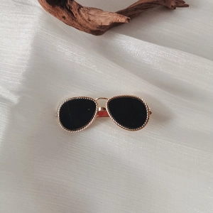 Close-up of golden aviator sunglasses with braided metal frames on white pleated fabric