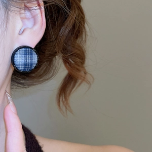 Close-up of blue plaid fabric stud earring worn on ear with round black frame detail