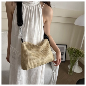 Detailed texture of hand-woven straw tote bag with black strap and silver chain detail