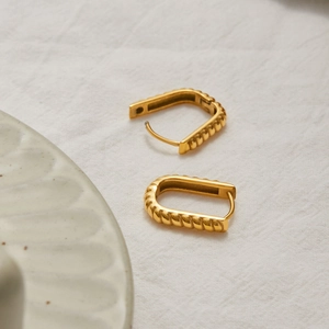 Detailed view of gold rectangular earrings with braided texture on a linen surface