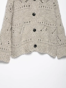 Detail of grey hollow knit cardigan with textured openwork patterns and black buttons