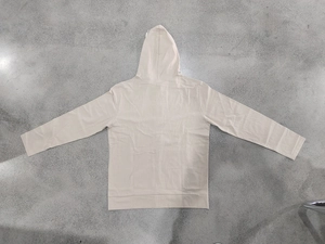 Detailed flat lay of beige linen hooded shirt showing fabric texture on concrete