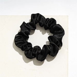 Detailed view of black satin scrunchie with soft elastic pleated texture on white block