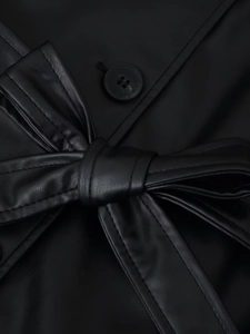 Détail de la veste en similicuir noir montrant la taille ceinturée et le bouton