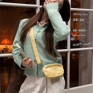 Gelbe Umhängetasche mit Schleifenstickerei getragen zu einem grünen Strickpullover