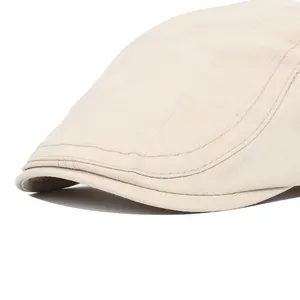 Detailed close-up of beige twill flat cap showing fine stitching and rounded brim texture