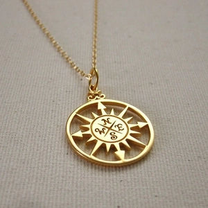 Macro detail of gold vintage compass pendant showing hollow design and NSEW engravings