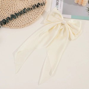 Close-up of a large beige satin bow hair clip with long ribbons on a white background