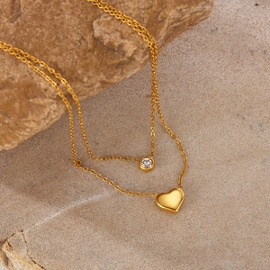 Detail of double-layer gold necklace featuring heart pendant and round zircon on stone
