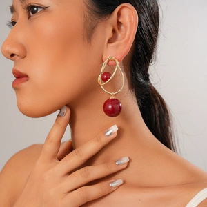 Detail of burgundy spherical drop earrings in gold finish on a model's ear