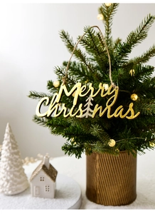 Detail of wooden Merry Christmas sign with gold glitter hanging on a lit Xmas tree