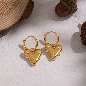 Boucles d'oreilles cœur dorées avec perles blanches sur un fond de texture naturelle