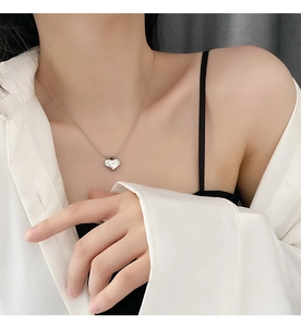 Detailed view of a silver heart pendant necklace on a model wearing a white shirt