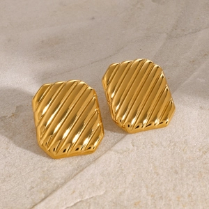 Macro shot of gold square earrings with wavy texture on a natural stone surface